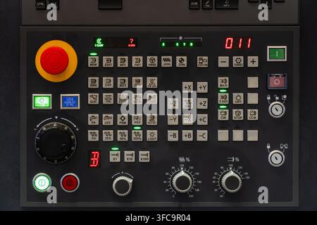 Industrial CNC lathe operator control panel with emergency stop button, rotary dials, function buttons, and LED displays Stock Photo