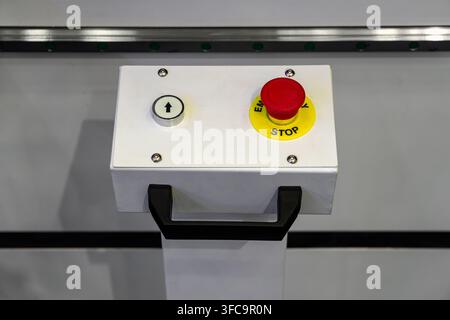White emergency stop control box featuring yellow safety collar, start button, and carrying handle on industrial machinery Stock Photo
