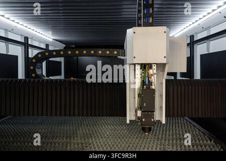 Industrial fiber laser cutting head assembly with energy chain track over serrated metal workbench inside enclosure Stock Photo