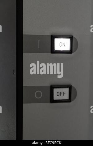 Modern power switch panel featuring square illuminated ON button and OFF button on dark grey metallic housing Stock Photo