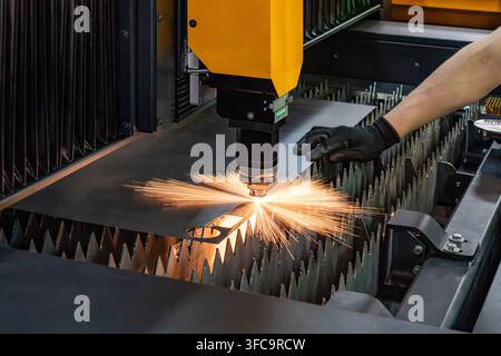 CNC fiber laser cutting machine cutting sheet metal with bright sparks burst while operator holds steel plate Stock Photo