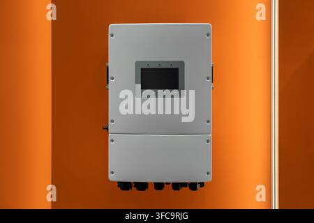 White hybrid solar inverter unit with cooling fans and DC switch installed on an illuminated orange wall Stock Photo