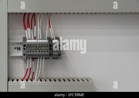Electrical terminal block mounted on DIN rail inside control cabinet with numbered connections, red and white wires Stock Photo