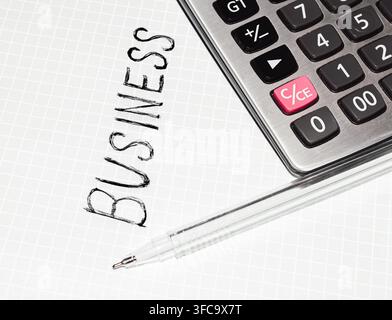 Business word written on grid paper beside calculator and pen. Calculator shows numeric keys and clear display Stock Photo