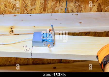 Contractor is installing an electrical box on wooden beam in building under construction Stock Photo