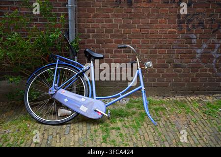 Delft, Netherlands - 07.04.2026 An abandoned blue bicycle leans against a brick wall on a cobblestone ground, embodying the essence of urban decay and Stock Photo