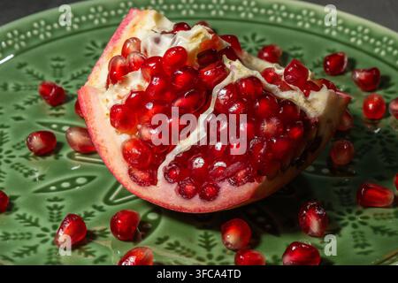 A close-up shot shows a ripe pomegranate cut open into sections, revealing its vibrant red arils on a green plate. Stock Photo