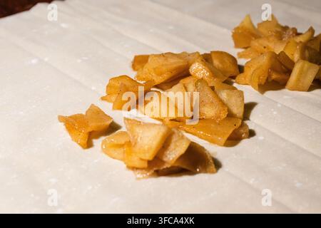 A close-up shot shows heaps of sweet, cooked apple pieces placed on sheets of raw phyllo dough or pastry ready for rolling. Stock Photo