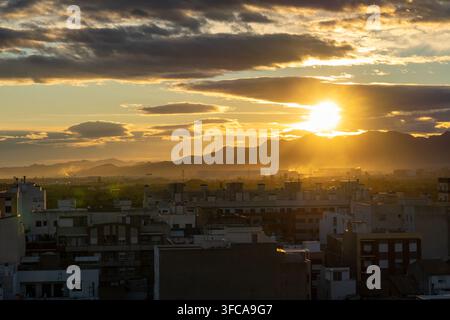 A dramatic sunset illuminates the sky with scattered clouds over ...