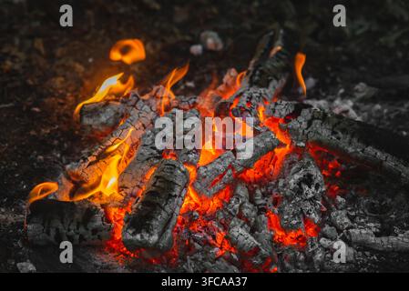 Campfire burning with glowing embers and small sparks in the dark, wilderness camping and adventure concept. Stock Photo