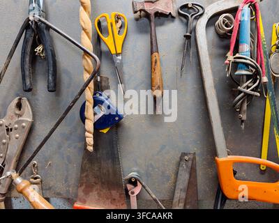 Various dirty and well used hand tools, including saws, pliers, hammers, and measuring tape, hanging neatly on a dusty workshop wall, representing cra Stock Photo