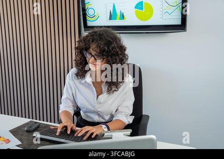 Businesswoman working on computer, analyzing data charts and graphs displayed on a screen Stock Photo