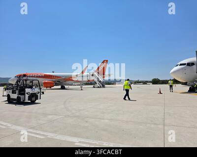 An easyJet Airbus passenger aircraft parked on an airport apron next to ground support equipment and staff working under a clear blue sky Stock Photo