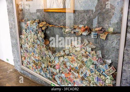 A glass storefront wall densely covered with colorful banknotes piled in a broad arc, creating a chaotic yet artistic money sculpture inside a gallery Stock Photo