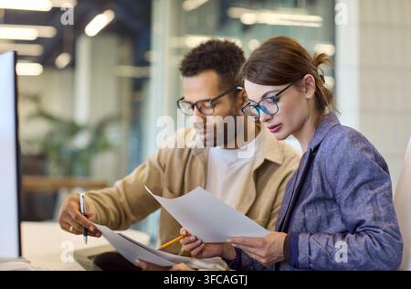 Focused coworkers analyzing papers together at desk in contemporary office Stock Photo