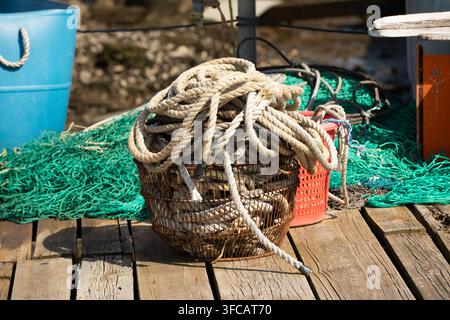 Closeup of Fishing Nets and Ropes Tied on an Old Wooden Dock by a Sailboat in a Harbor, Nautical Mooring Lines and Rigging by the Sea Stock Photo