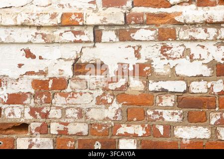 Damaged antique red brick wall with peeling white plaster texture. Stock Photo
