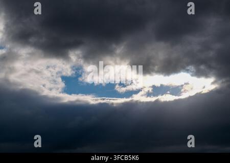 Dramatic skyscape of sun rays breaking through heavy dark storm clouds revealing a patch of clear blue sky in Siena, Tuscany, Italy. Concept for hope Stock Photo