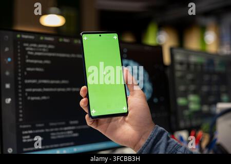 Close up of system administrator using green screen smartphone, debugging app issues and improving system stability. IT expert in tech company office Stock Photo