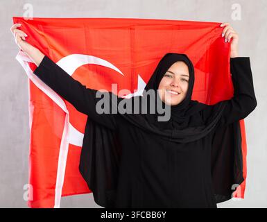 Cheerful young muslim woman wearing black traditional hijab holding flag of turkey Stock Photo