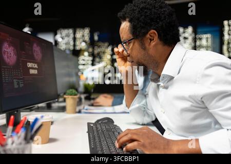 Software developer adjusting glasses, surprised by application errors while coding. African american man troubled by computer bugs while coding in sof Stock Photo