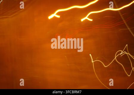 An abstract long exposure shot featuring vibrant yellow and red light trails dancing motion across a warm, textured orange background. Stock Photo