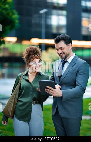 Business professionals collaborating outdoors, using digital tablet for work Stock Photo