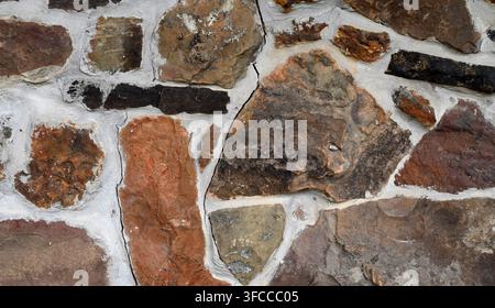 Close up of a multi color rock and mortar wall surface with porous, rough uneven stones and several large cracks Stock Photo