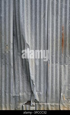 Corrugated galvanized tin metal panel siding with a large wrinkle, rust and weatherworn surface damage in a vertical view Stock Photo