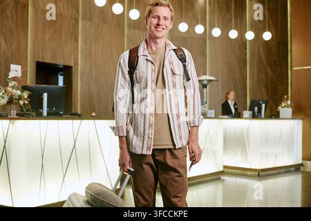 Portrait of Smiling Man with Suitcase Standing in Hotel Lobby Stock Photo