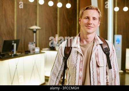 Portrait of Smiling Man with Backpack Standing in Hotel Lobby Stock Photo