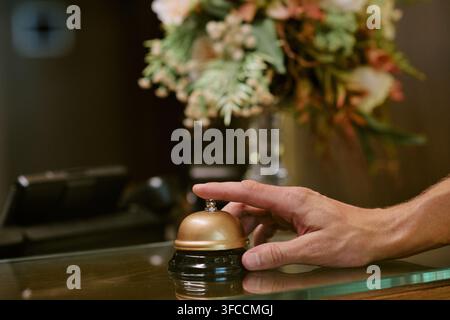 Man Pressing Service Bell on Reception Desk in Hotel Lobby Stock Photo