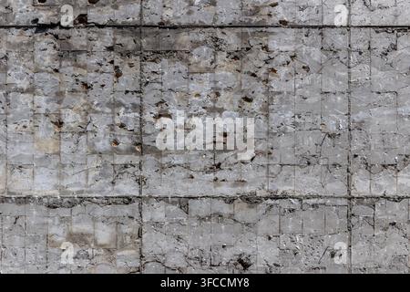 Close-up view of a weathered concrete wall with visible damage. Textured surface features cracks, chips, and exposed rebar, highlighting decay and dis Stock Photo