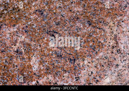 Close-up view of a rough granite stone surface with mottled reddish-brown, gray, black, and white mineral grains. Natural lighting highlights the text Stock Photo