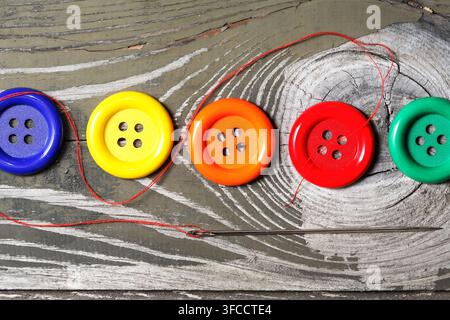 Several buttons of different types and a needle with thread on an old wooden table Stock Photo
