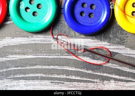 Several buttons of different types and a needle with thread on an old wooden table Stock Photo