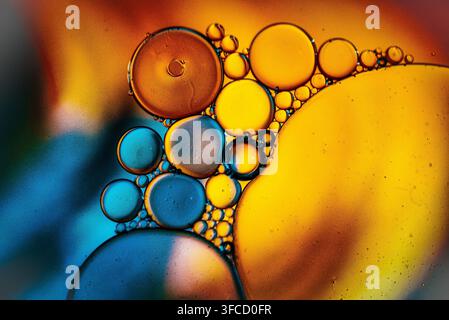 Abstract macro photograph of colourful oil and water droplets forming circular patterns in orange, yellow and blue, photographed in Copthorne, West Su Stock Photo