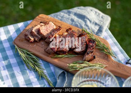 Freshly grilled juicy beef steak sliced and served on a rustic wooden board on an outdoor garden picnic table, creating an appetizing summer barbecue Stock Photo