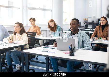 Education, Technology, Lifestyle And People Concept. Group of diverse international students sitting at desk in classroom using laptop computers, stud Stock Photo