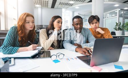 Studying Together. Focused diverse multiracial students sitting at desk in auditorium using laptop, watching tutorial or educational video, doing rese Stock Photo