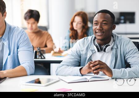 Back To Highschool. Portrait of interested black student sitting at desk with multicultural classmates, listening to teacher. Diverse people studying Stock Photo