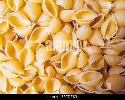 Close-up and background of dry uncooked conchiglie shell pasta, yellow food texture. Stock Photo