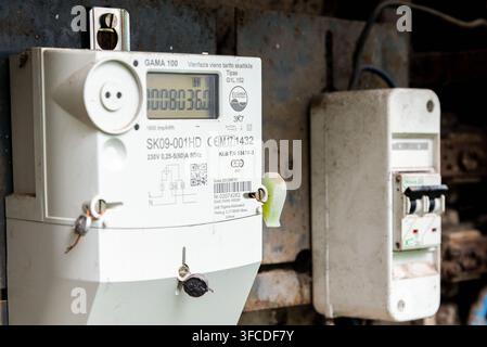 Old digital electric meter and circuit breaker mounted on a weathered industrial panel with rusty metal structures, showing energy usage measurement a Stock Photo