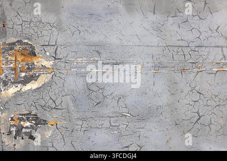 Close-up of a weathered metal surface showcasing peeling gray paint and rust. Extensive cracking and chipping reveal dark layers and orange rust patch Stock Photo