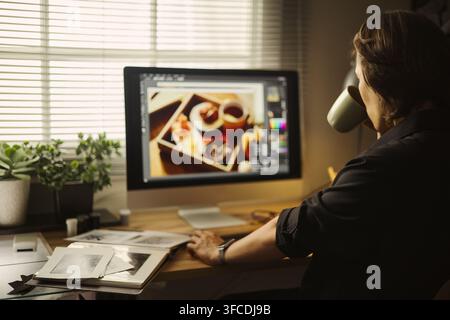 Caucasian young woman working on computer, editing photos and drinking coffee. Image suitable for remote work, freelance graphic design, and creative agency marketing campaigns Stock Photo