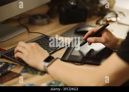 Hands of male designer using graphics tablet and keyboard at wooden desk. Image represents digital art creation, suitable for creative agency marketing Stock Photo
