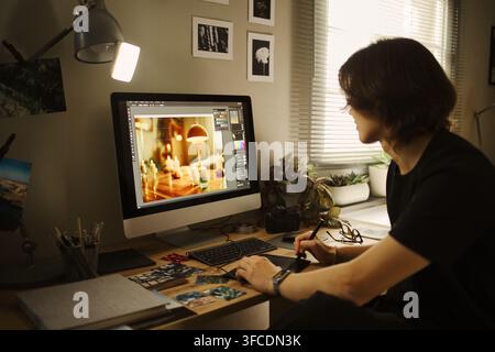 Young Asian man editing photo on computer using graphics tablet at home office. Image represents remote work and creative profession, suitable for freelance career marketing Stock Photo