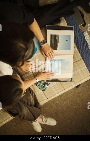 High angle view of young couple looking at photo album together, reminiscing about travel memories. Image is suitable for family lifestyle and print service marketing, vertical Stock Photo