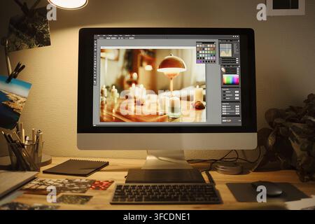 Desktop computer displaying photo editing software on screen in creative home office workspace. Image ideal for promoting digital design courses and photography post-production services Stock Photo
