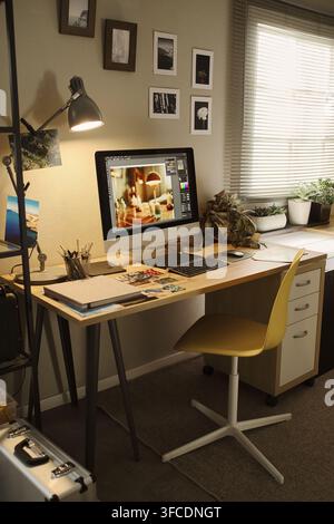 Vertical image of creative home office workspace featuring computer monitor displaying photo editing software. Scene represents remote work and digital design career marketing Stock Photo